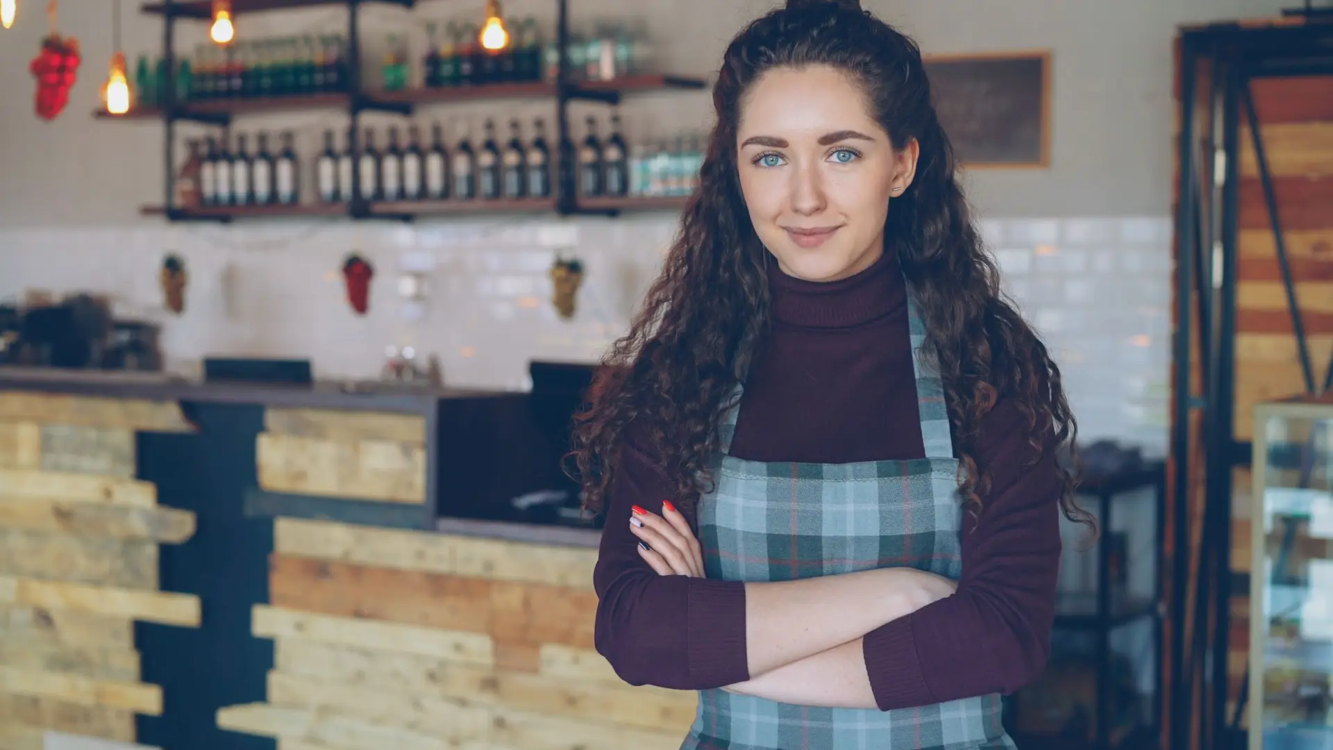 A café owner in an apron smiling in her coffee shop