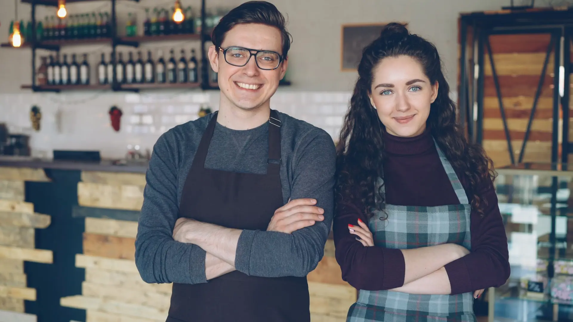 Two café owners in aprons smiling behind their counter
